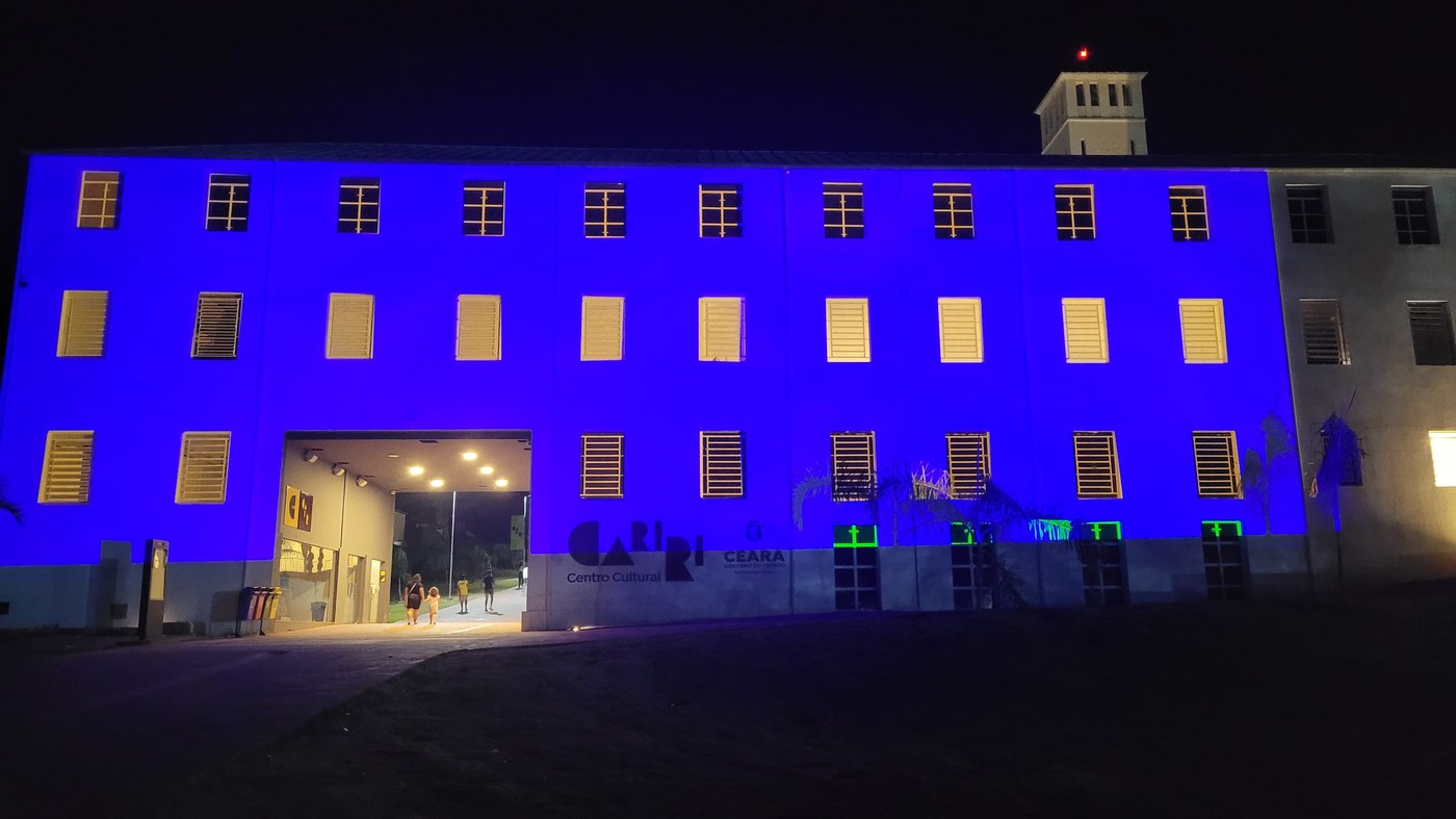 Vista ampla da fachada inteira mapeada em azul sólido, com a torre do prédio ao fundo
