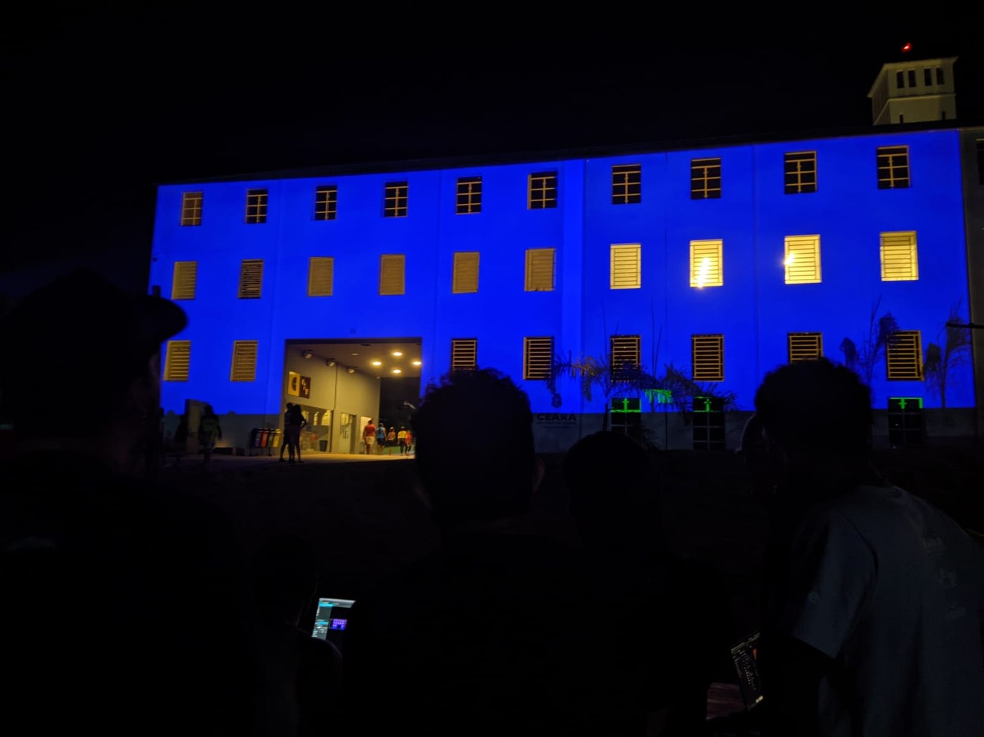 Silhuetas da turma em primeiro plano com a fachada azul ao fundo