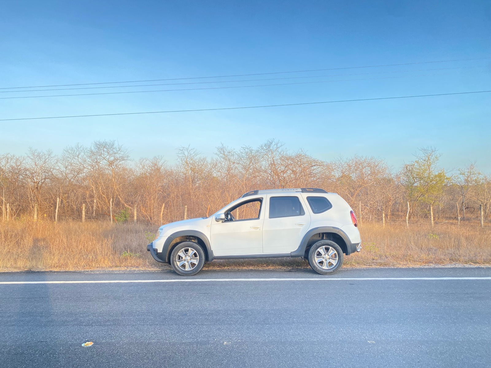 Carro parado na beira da estrada, vegetação seca do sertão ao fundo