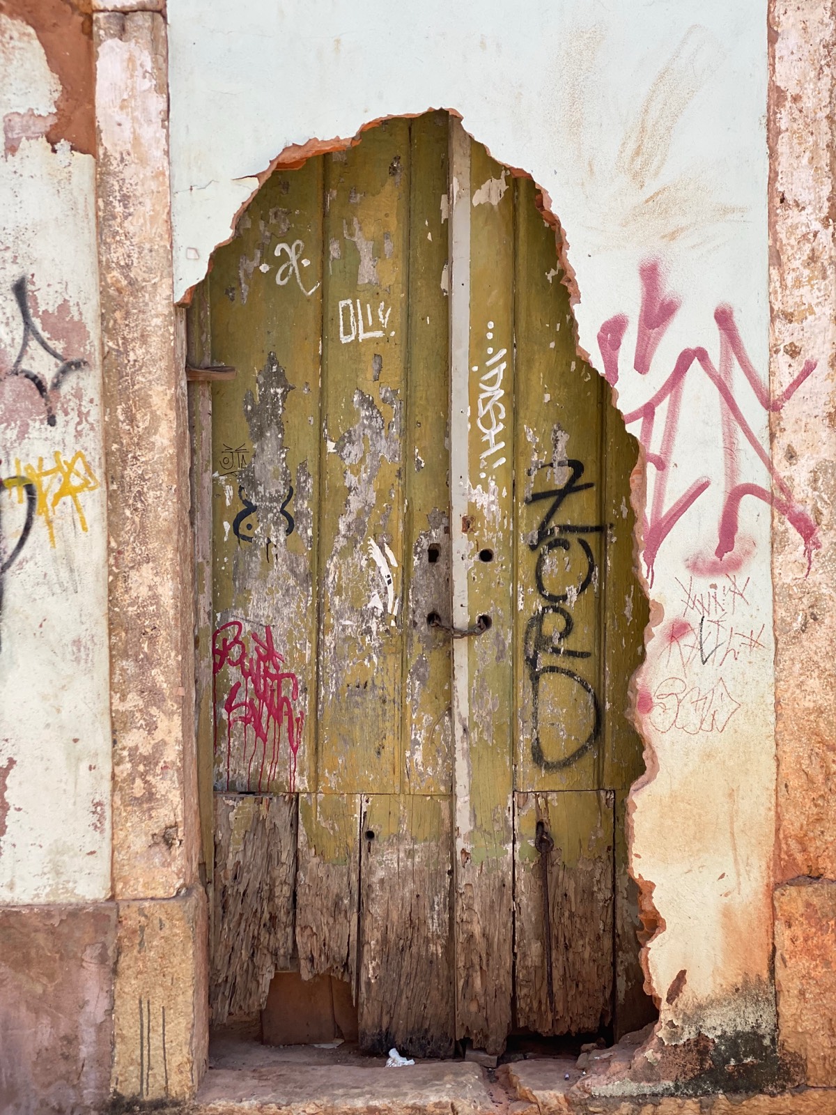 Porta antiga em arco, de madeira degradada, coberta de grafite
